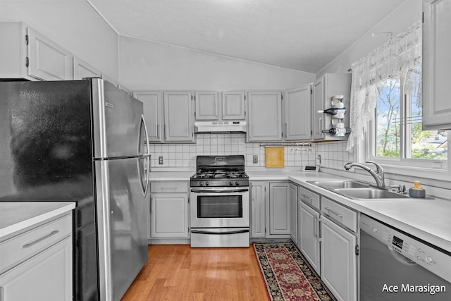 kitchen with appliances with stainless steel finishes, a sink, vaulted ceiling, under cabinet range hood, and light wood-style flooring