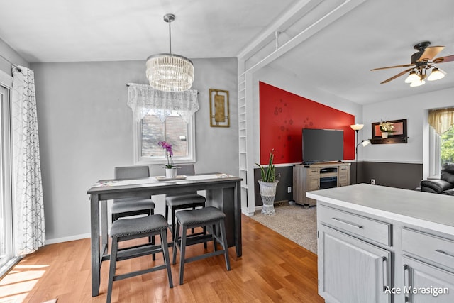 dining room with light wood-style floors, ceiling fan, a chandelier, and baseboards