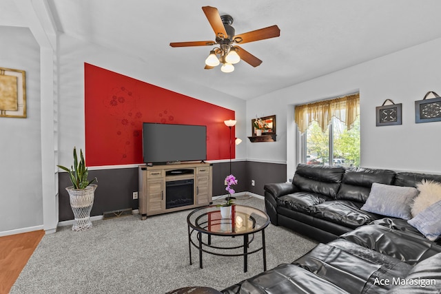 living room featuring ceiling fan, baseboards, wood finished floors, and an accent wall