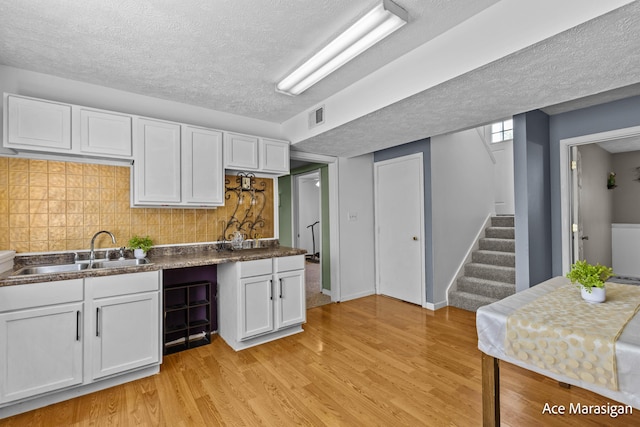 kitchen featuring a sink, a textured ceiling, white cabinets, light wood finished floors, and dark countertops