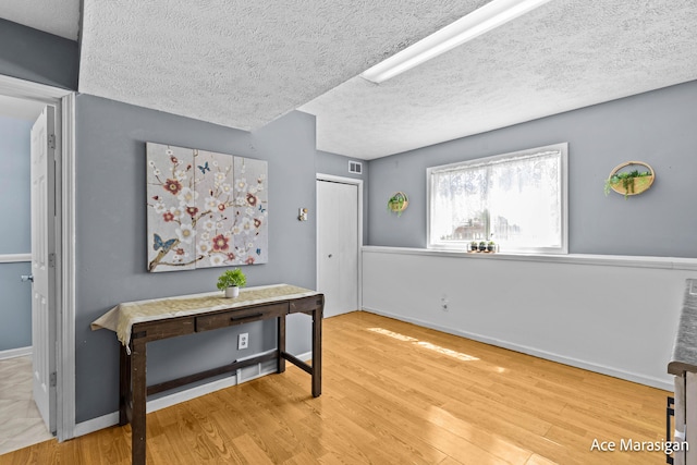 corridor featuring wood finished floors, baseboards, and a textured ceiling