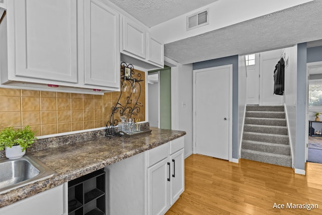 kitchen with a textured ceiling, white cabinets, light wood finished floors, tasteful backsplash, and dark countertops