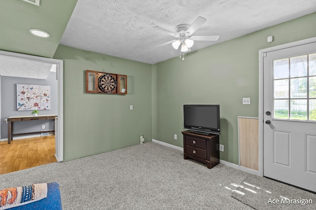unfurnished living room featuring a ceiling fan, a textured ceiling, baseboards, and carpet flooring