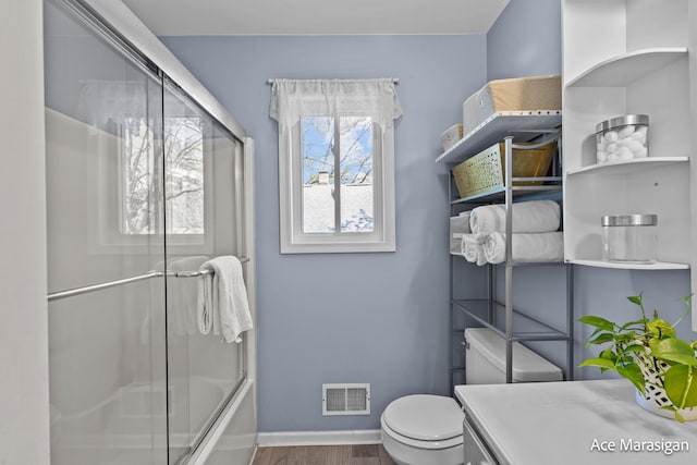 bathroom featuring wood finished floors, baseboards, toilet, combined bath / shower with glass door, and vanity