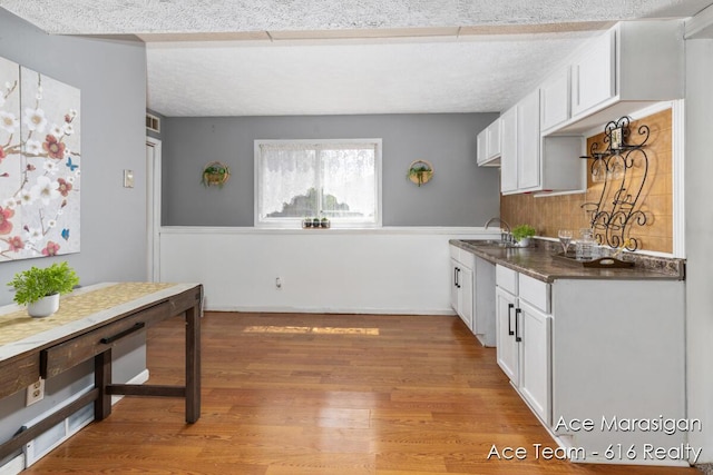 kitchen featuring white cabinetry, dark countertops, light wood-type flooring, and a sink