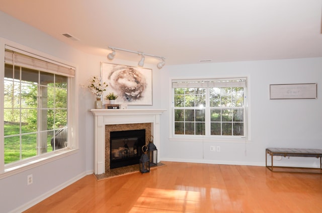 unfurnished living room featuring rail lighting, wood finished floors, a fireplace with flush hearth, and plenty of natural light