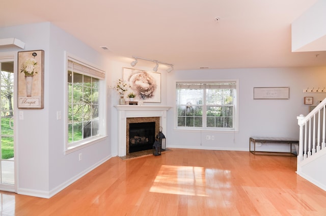 unfurnished living room with wood finished floors, track lighting, a fireplace with flush hearth, baseboards, and stairs