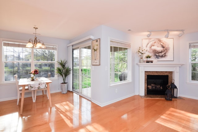 living area with rail lighting, wood finished floors, a fireplace with flush hearth, a chandelier, and baseboards