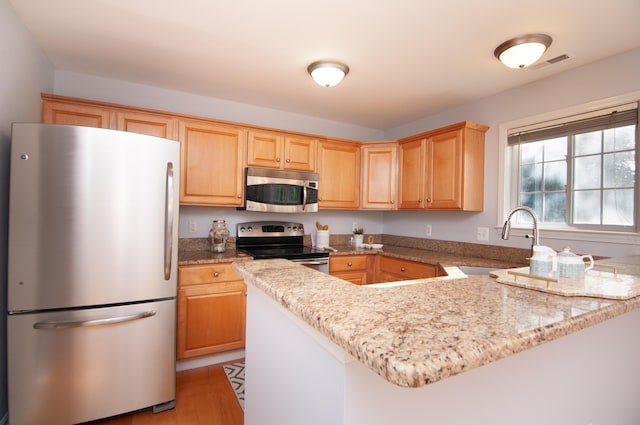 kitchen with appliances with stainless steel finishes, a sink, light brown cabinets, and a peninsula
