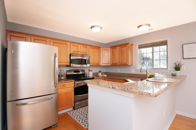 kitchen featuring stainless steel appliances, a sink, a peninsula, and light wood-style floors