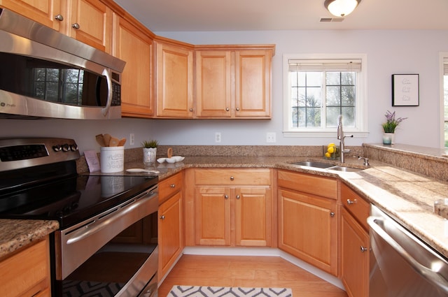 kitchen with stainless steel appliances, a sink, light wood-style flooring, and light stone counters