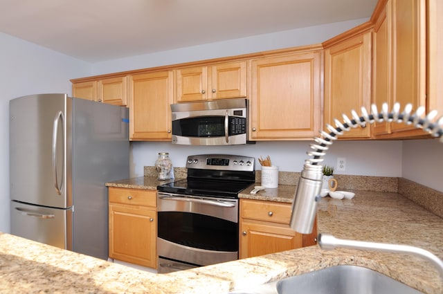 kitchen featuring appliances with stainless steel finishes, light stone countertops, and light brown cabinetry