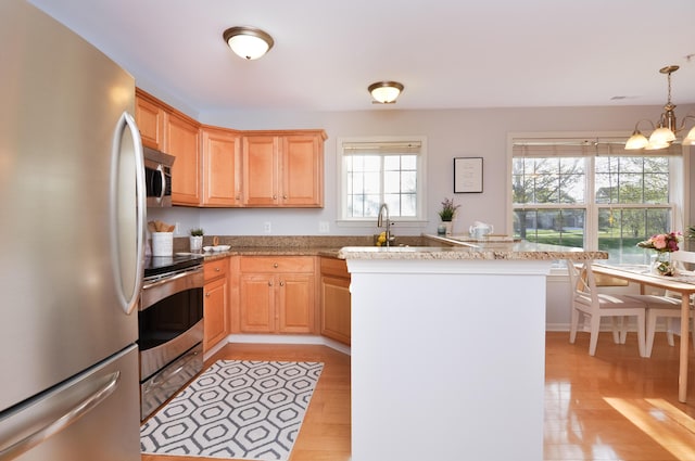kitchen featuring appliances with stainless steel finishes, a chandelier, light wood-style floors, light brown cabinets, and decorative light fixtures