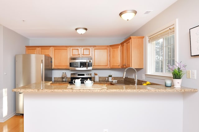 kitchen featuring stainless steel appliances, a peninsula, light stone countertops, light wood-type flooring, and a sink
