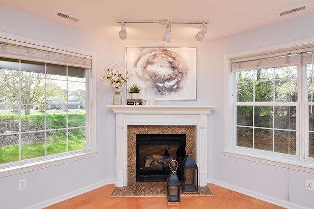 detailed view of wood finished floors, rail lighting, baseboards, and a fireplace with flush hearth