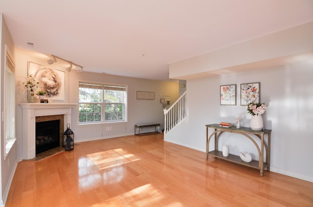 unfurnished living room with wood finished floors, stairway, a fireplace with flush hearth, baseboards, and rail lighting