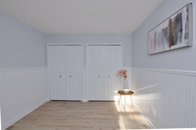 unfurnished bedroom featuring two closets, a wainscoted wall, and wood finished floors