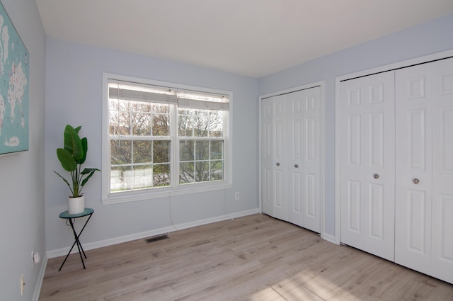 unfurnished bedroom with two closets, light wood-type flooring, and baseboards