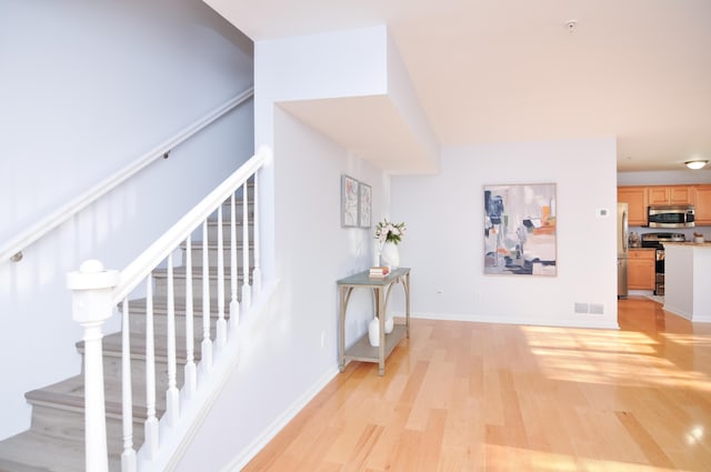 corridor with light wood-style floors, stairway, and baseboards