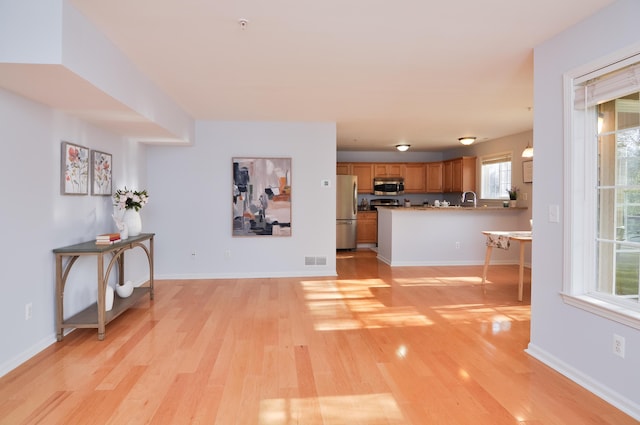 unfurnished living room featuring light wood-style floors, a sink, and baseboards
