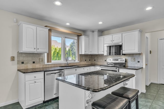 20261 Ramblewood Dr, Macomb, MI 48044 - kitchen featuring appliances with stainless steel finishes, a sink, white cabinetry, dark stone countertops, and a breakfast bar