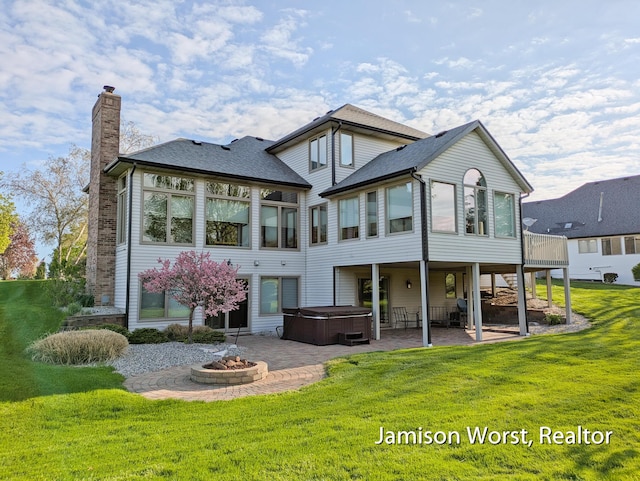 back of house featuring a hot tub, a chimney, a patio, a lawn, and a fire pit