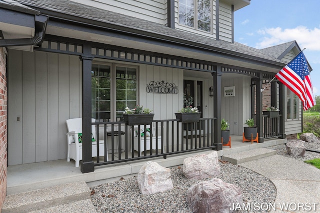 doorway to property with covered porch and a shingled roof