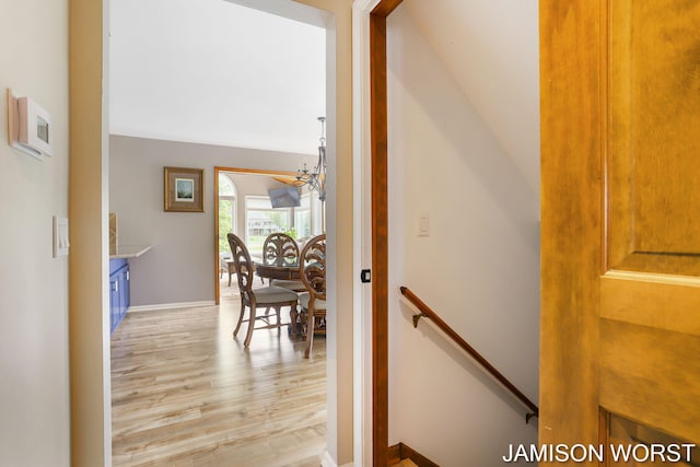 hall with light wood-type flooring, an upstairs landing, and a chandelier