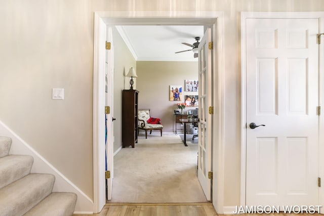 hall with crown molding, baseboards, stairs, light wood-type flooring, and light colored carpet