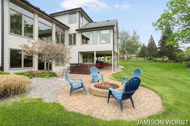 back of house with a hot tub, a patio area, a yard, and an outdoor fire pit