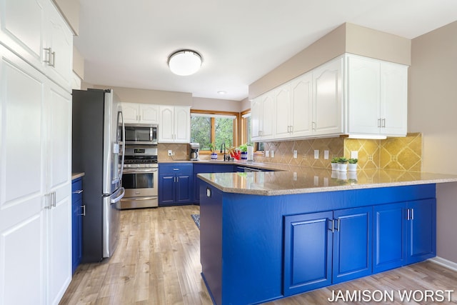 kitchen with stainless steel appliances, blue cabinetry, a peninsula, white cabinetry, and light wood finished floors