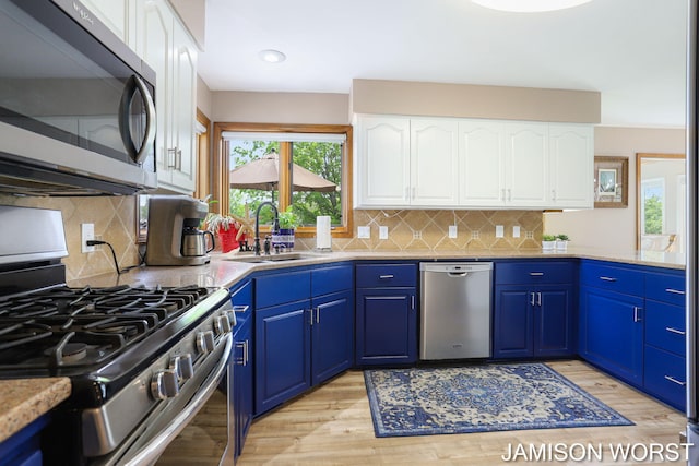 kitchen featuring appliances with stainless steel finishes, a sink, light wood finished floors, white cabinets, and recessed lighting