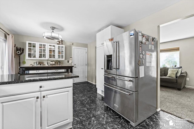 kitchen with stainless steel fridge, white cabinetry, glass insert cabinets, baseboards, and dark stone counters