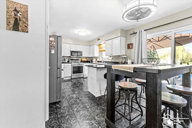 kitchen featuring appliances with stainless steel finishes, white cabinetry, a sink, and dark countertops