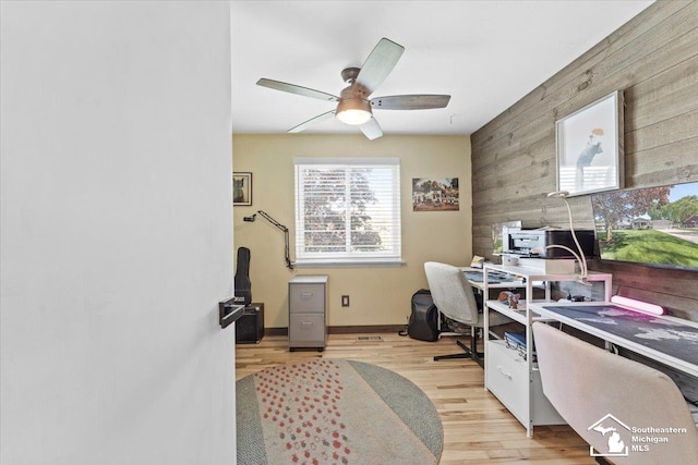 office area featuring wooden walls, ceiling fan, light wood-type flooring, an accent wall, and baseboards