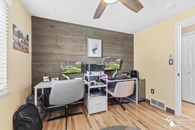 office area featuring wooden walls, an accent wall, light wood-style floors, a ceiling fan, and baseboards