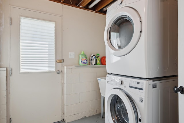 laundry room with stacked washer and clothes dryer and concrete block wall