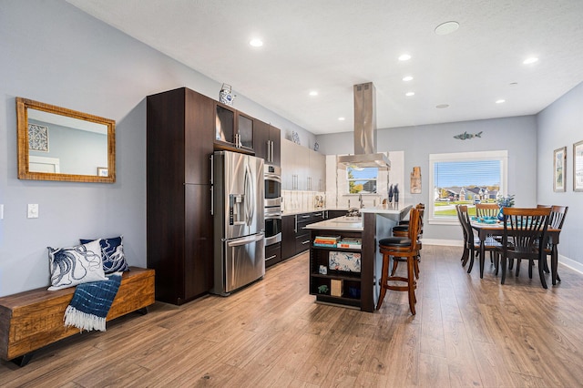 3080 Silver Fir Ct, Holland, MI 49424 - kitchen with appliances with stainless steel finishes, island range hood, light wood finished floors, dark brown cabinets, and a breakfast bar