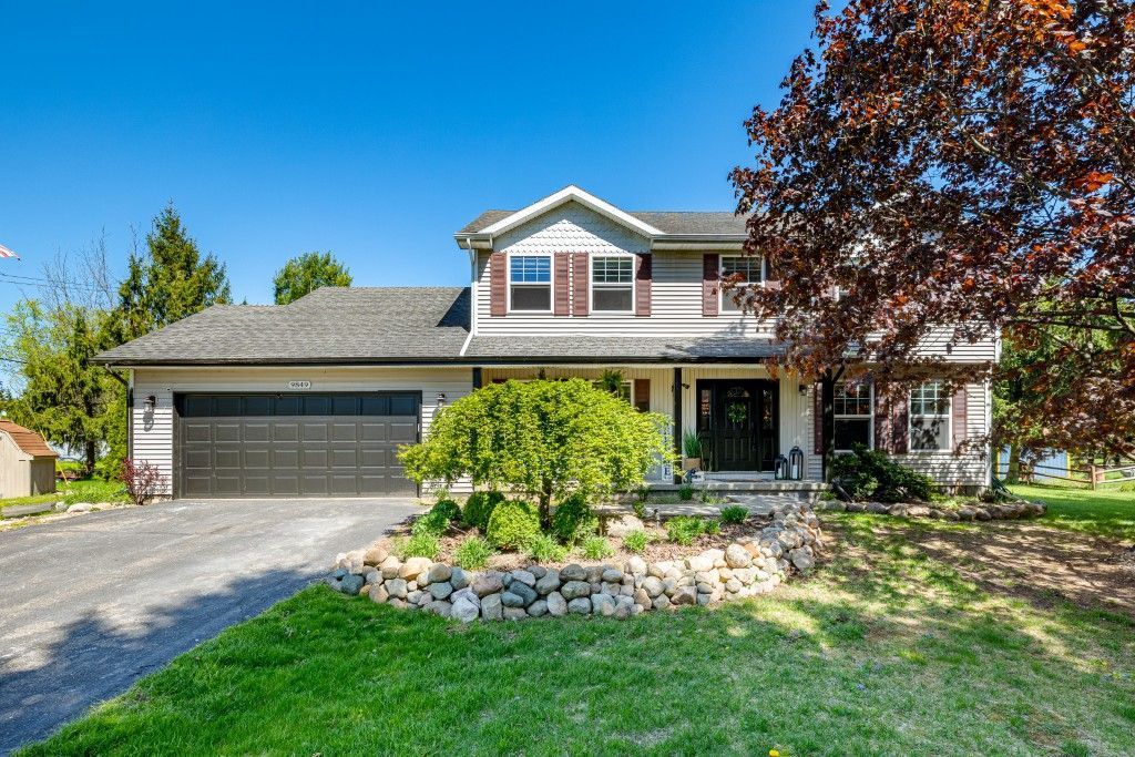 9849 Marshall Rd, South Lyon, MI 48178 - traditional-style house featuring an attached garage, asphalt driveway, a front lawn, covered porch, and a shingled roof