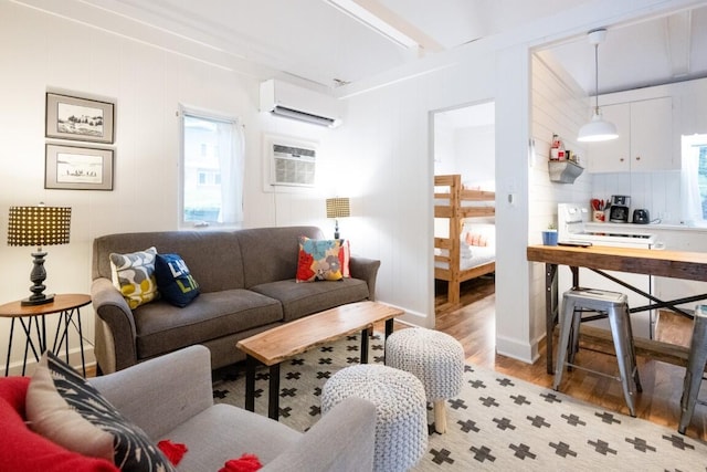 living room with an AC wall unit, light wood-type flooring, beamed ceiling, and a wall unit AC