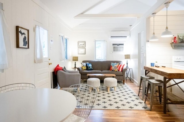 living room with an AC wall unit, wood finished floors, a wall mounted AC, and beamed ceiling
