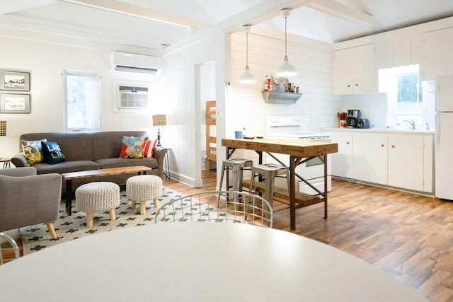 kitchen featuring white appliances, an AC wall unit, light wood-style floors, white cabinetry, and beamed ceiling