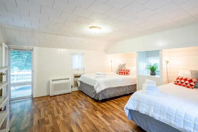 bedroom featuring multiple windows, wood finished floors, access to exterior, heating unit, and lofted ceiling