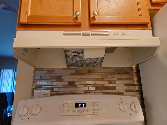 kitchen view of under cabinet range hood, stove, a smoke detector, and decorative backsplash