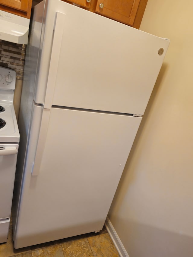 kitchen view of freestanding refrigerator, range hood, range with electric stovetop, and brown cabinetry