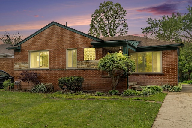 view of front facade with brick siding, a front lawn, and roof with shingles