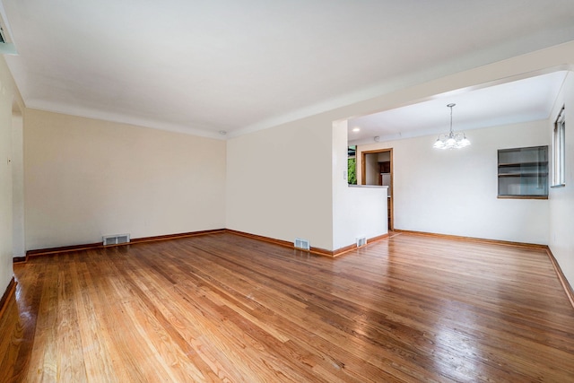 unfurnished room featuring a chandelier, hardwood / wood-style flooring, and baseboards