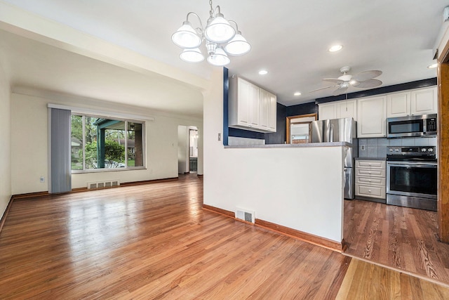 kitchen featuring appliances with stainless steel finishes, white cabinetry, wood finished floors, a chandelier, and baseboards