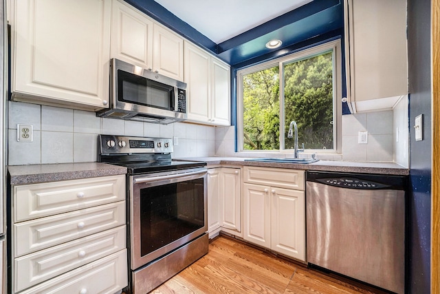 kitchen with stainless steel appliances, a sink, light wood-style flooring, and white cabinetry