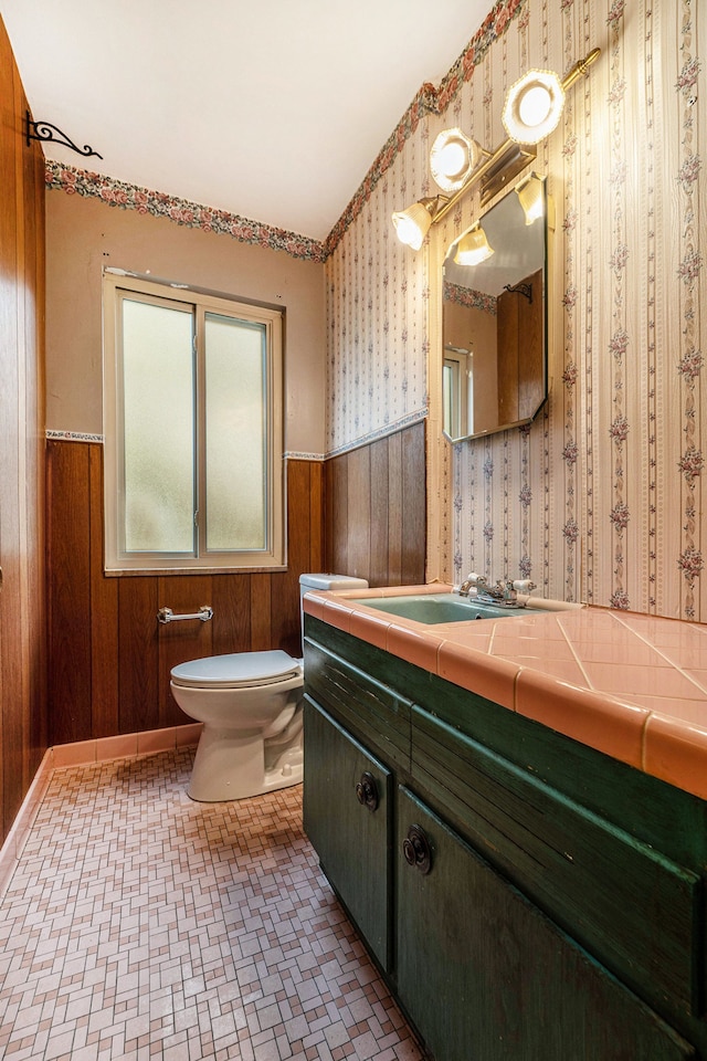 half bathroom featuring a wainscoted wall, wallpapered walls, toilet, wood walls, and vanity